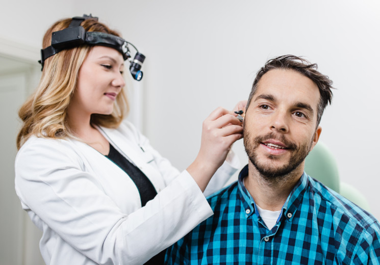 A female audiologist examines a male patient's ear for hearing loss